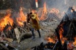 In India, a man runs past the flames of a mass cremation. Mass cremations have started in neighbouring Sri Lanka. Photo: CNS photo/Adnan Abidi, Reuters