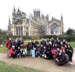 Large group of people posing for a group photo in front of a historic Gothic cathedral with pointed arches and tall spires.
