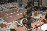 Dozens of priests lie prostrate on a red carpet in a grand church during a solemn liturgical ceremony, with clergy and attendees surrounding them.