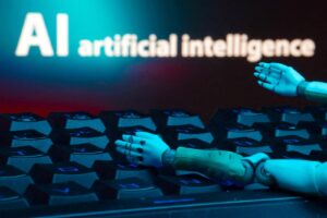 Robotic hands rest on a keyboard as a blue glow and the words 'AI artificial intelligence' appear on a screen in the background.