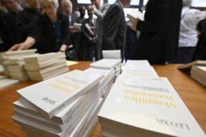 Stacks of white books on a wooden table at a crowded event, attendees browsing in the background.