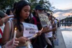 Group of protesters at dusk holding candles; foreground woman reads a paper with the Filipino message 'ITIGIL ANG MILITARISASYON SA NEGROS'.