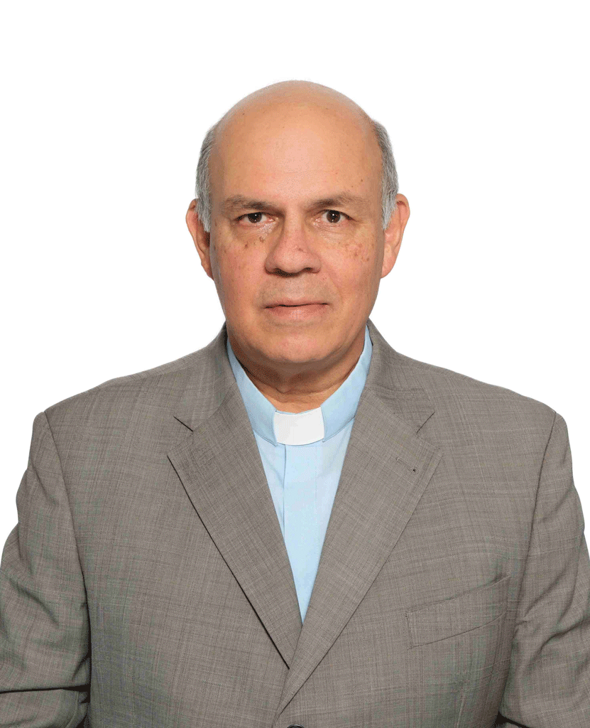 Portrait of a middle-aged priest in a gray suit and light blue clerical shirt against a white background, looking at the camera.] ,