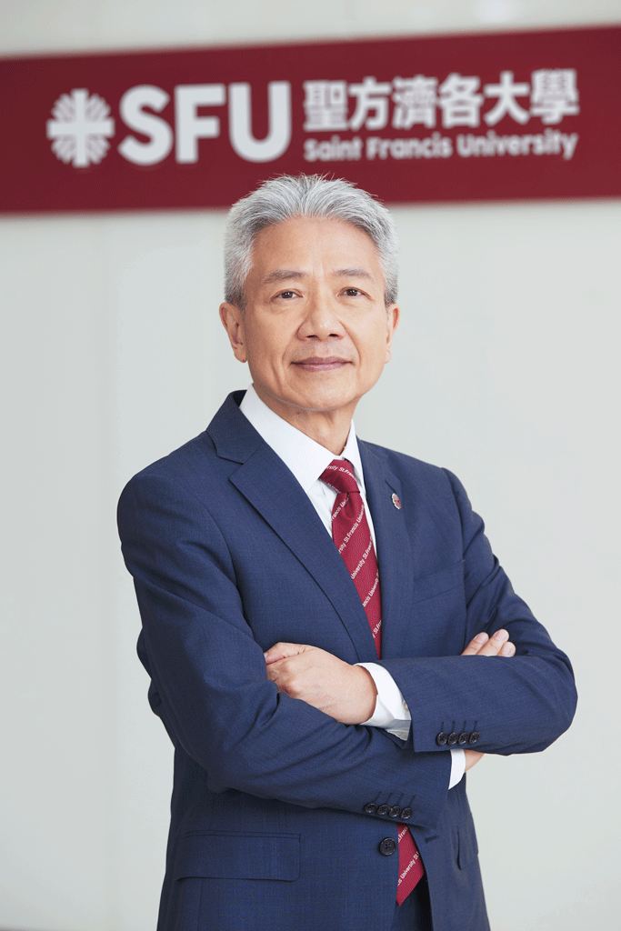 Professional portrait of an older man in a navy suit with a red tie, arms crossed, in front of an SFU sign (Saint Francis University).