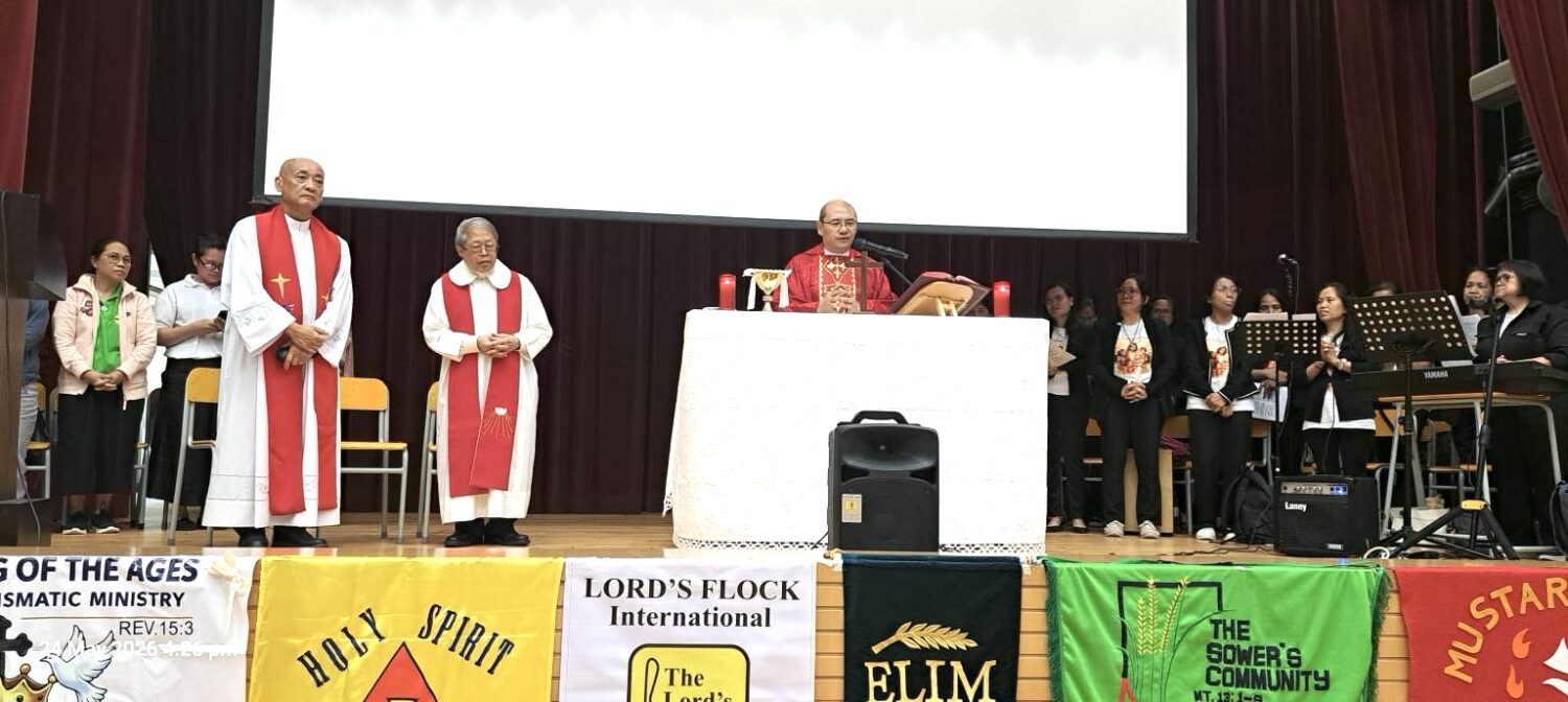 Priests in white robes with red stoles lead a church service on a stage with a choir in the background.