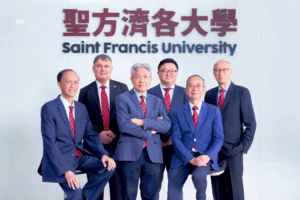 Six men in suits posing for a formal group photo in front of a Saint Francis University sign with Chinese characters above them.