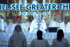 Bride and groom stand before an altar as a bishop and priests celebrate Mass from behind the couple