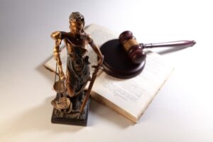 Statue of Lady Justice with scales and sword beside an open law book and gavel in the background.