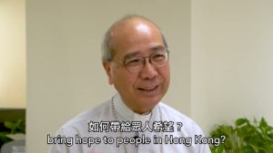 Elderly East Asian man with glasses in a clerical shirt speaks in an interview; caption reads 'bring hope to people in Hong Kong?'