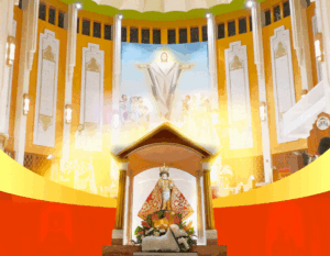 Central shrine with a statue in ornate red robes, surrounded by flowers, inside a colorful church with a mural of Jesus behind it.