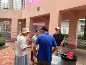 Four adults chatting outside a pink arched building, with a cleaning cart and cooler nearby on a brick courtyard. (informative)